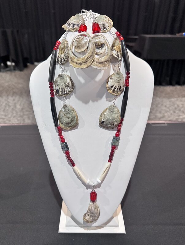 Earrings and a necklace made from Olympia oyster shells and red beads, on a white display bust